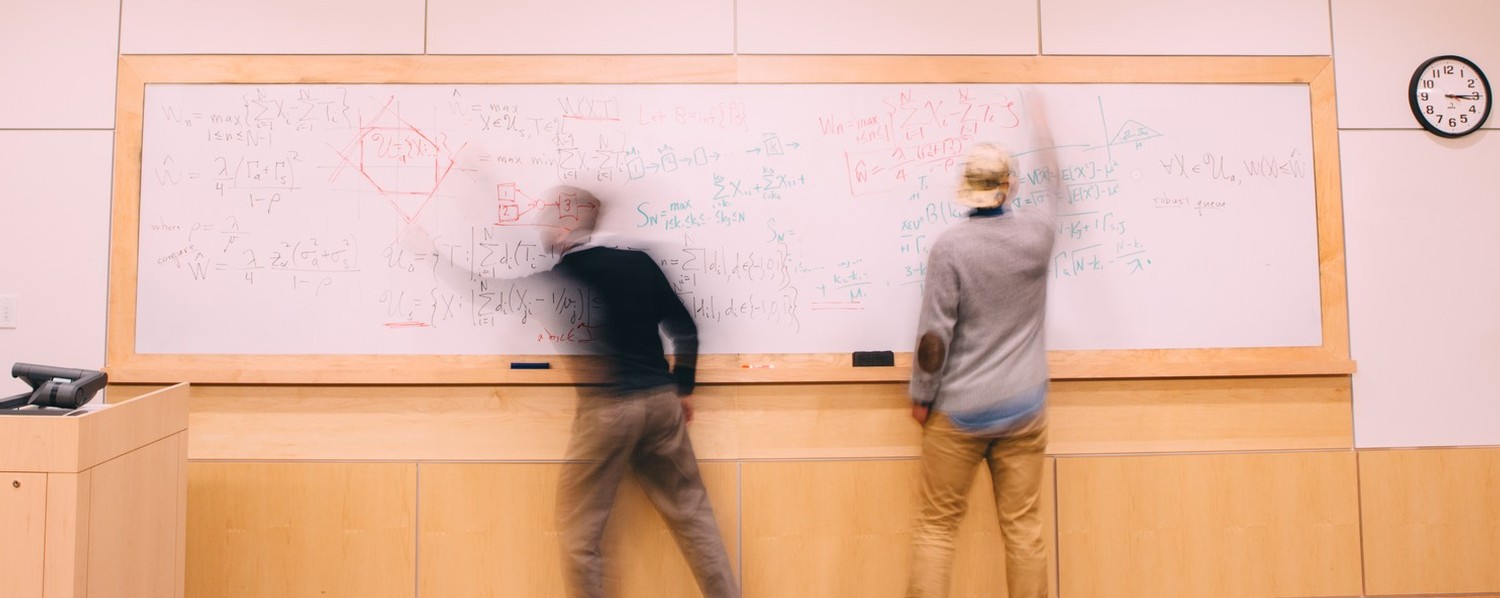 two math majors at Gordon College working through a math problem on a white board