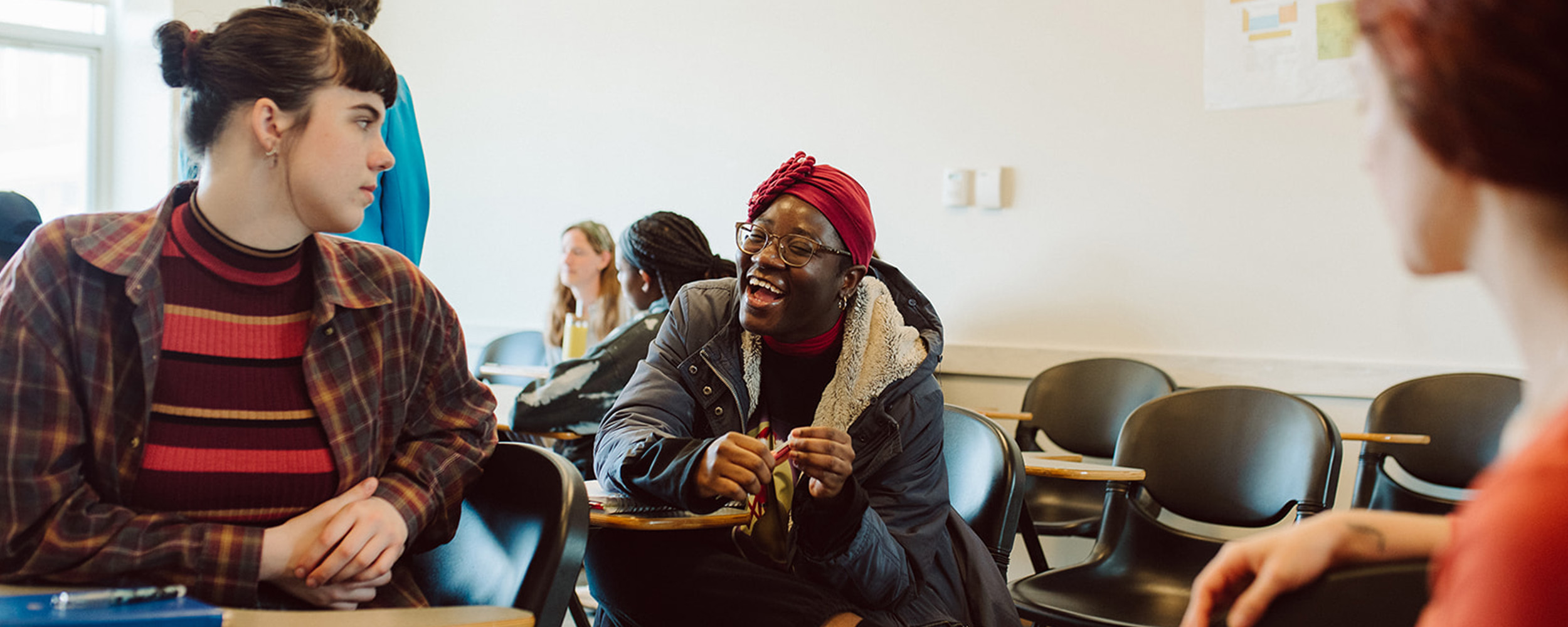 a group of three Gordon College students sitting in a classroom talking and laughing together