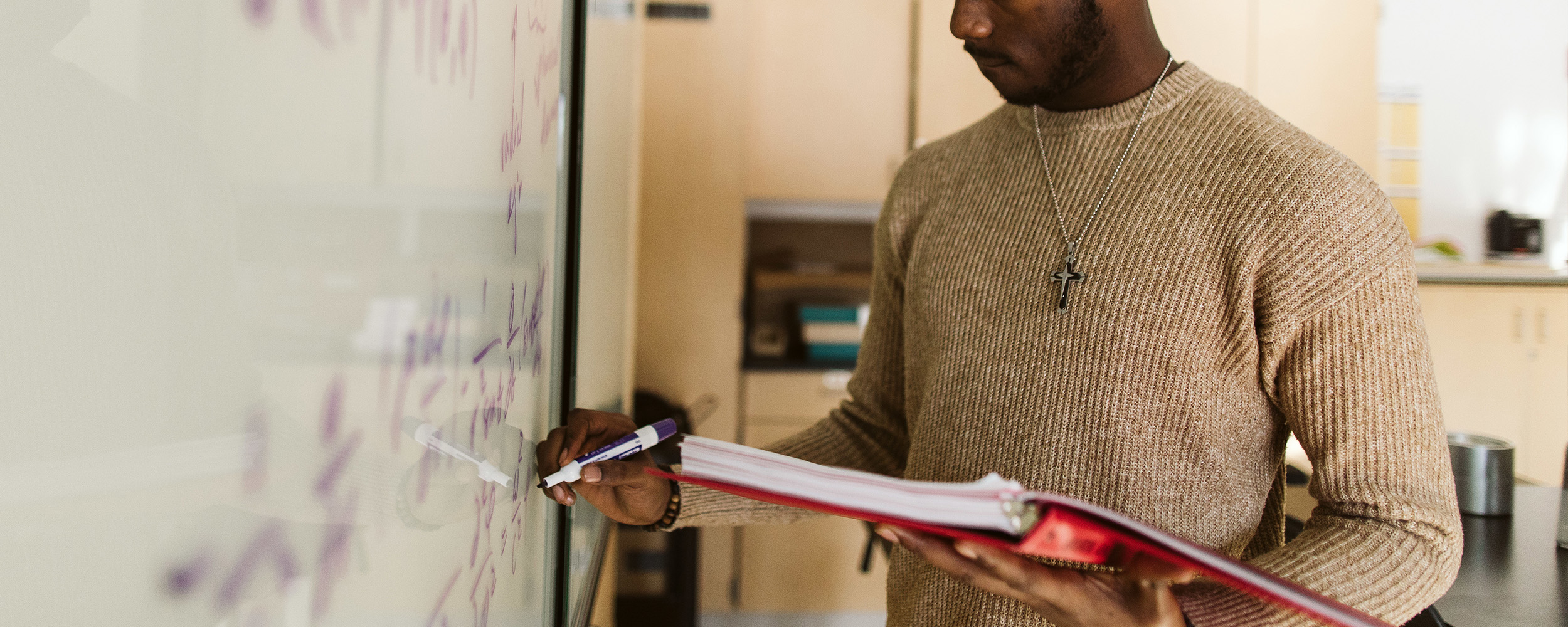 an engineering student at Gordon College holding a binder and writing on a white board