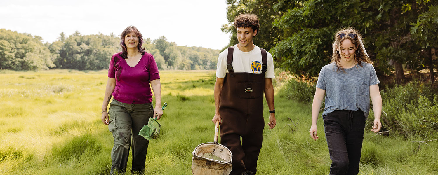 students in waders walking through marsh